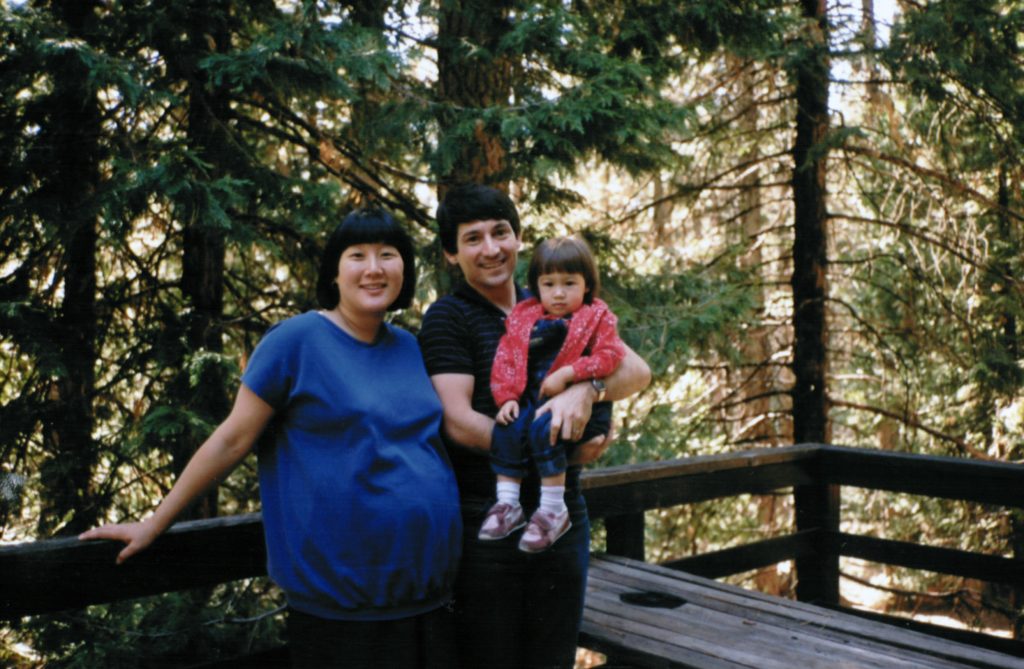 In a photo from the 1980s, a family poses among trees.