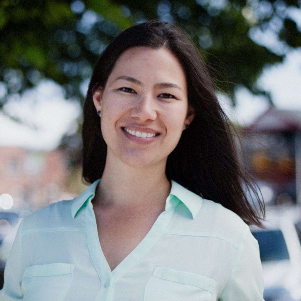 A woman with dark hair and a light blue shirt smiles for a portrait