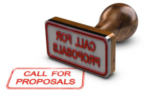 Rubber stamp with rounded wood handle lying on white background. "CALL FOR PROPOSAL" stamped in red.