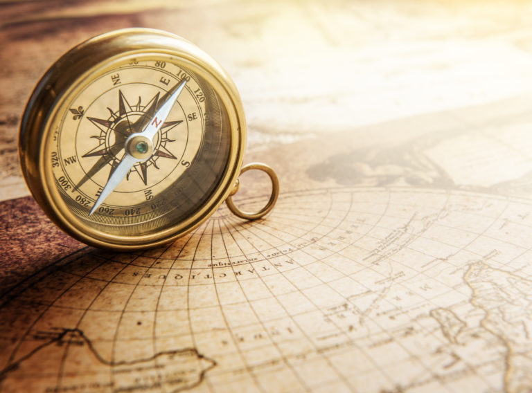 Gold vintage compass on its side sits on vintage map.