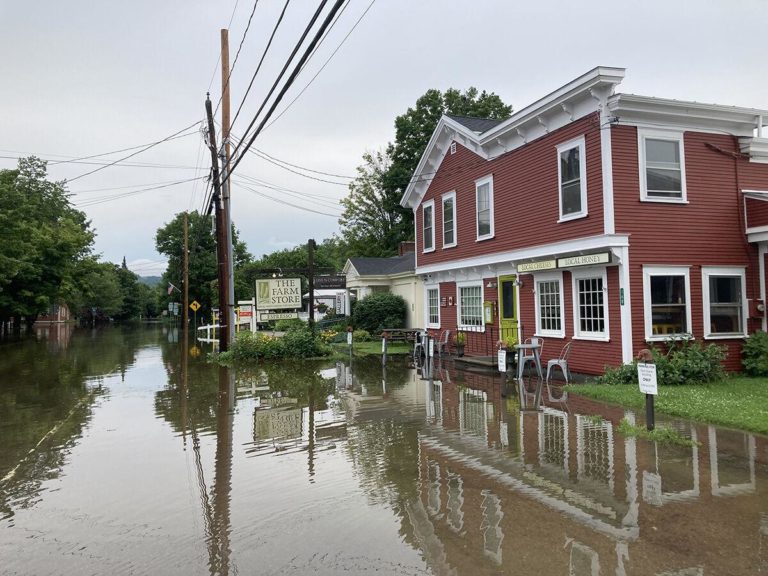 Color photo of flooded street with red farm store on right-hand side