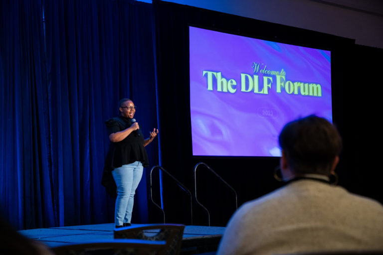 DLF Forum 2023 Keynote Kishonna Gray stands on stage next to large display featuring "The DLF Forum."