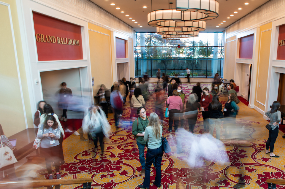 Time lapse color photo of conference goers moving around hotel lobby.