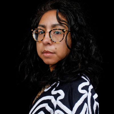 Headshot image of Jennifer Ferretti wearing black and white top against black background.